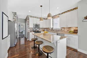 Kitchen featuring white cabinetry, pendant lighting, stainless steel appliances, a kitchen breakfast bar, and light stone countertops