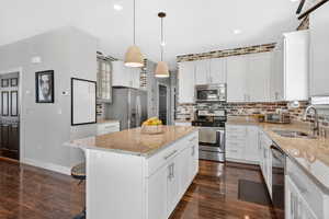 Kitchen with white cabinets, appliances with stainless steel finishes, decorative light fixtures, a kitchen island, and light stone countertops