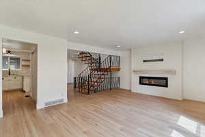 Unfurnished living room with a glass covered fireplace, light wood-type flooring, stairway, and recessed lighting