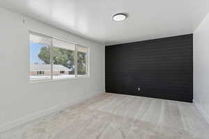 Empty room featuring light colored carpet, an accent wall, and wood walls