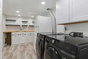 Laundry area with cabinet space, light wood-type flooring, separate washer and dryer, and recessed lighting