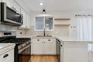 Kitchen featuring stainless steel appliances, light countertops, white cabinetry, a peninsula, and open shelves