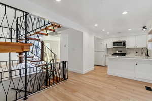 Kitchen featuring white cabinetry, stainless steel appliances, light wood-type flooring, decorative backsplash, and recessed lighting