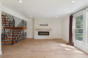 Unfurnished living room featuring stairs, light wood-style flooring, a glass covered fireplace, and recessed lighting