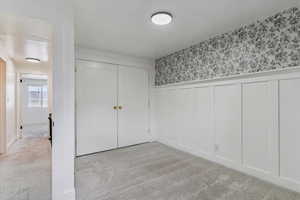 Unfurnished bedroom featuring a wainscoted wall, light carpet, a closet, a decorative wall, and wallpapered walls