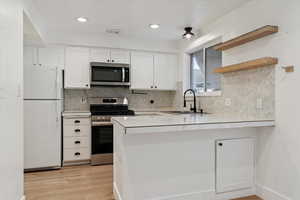 Kitchen featuring stainless steel appliances, white cabinetry, a peninsula, open shelves, and light wood-style flooring