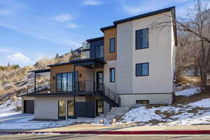 Snow covered rear of property featuring stucco siding, a garage, and stairs