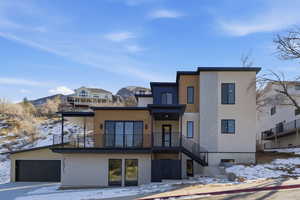 Snow covered rear of property with stucco siding, a garage, a balcony, stairs, and a mountain view