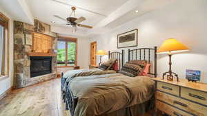 Bedroom with a large fireplace, wood-type flooring, ceiling fan, a tray ceiling, and recessed lighting