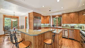 Kitchen featuring pendant lighting, a raised ceiling, light wood-style floors, a kitchen bar, and tasteful backsplash