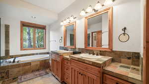 Full bathroom featuring two vanities, a garden tub, and light stone finish flooring