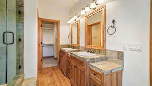 Full bathroom with two vanities, light wood-style flooring, a shower stall, and a spacious closet