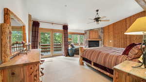 Bedroom with vaulted ceiling, access to exterior, a fireplace, wooden walls, and carpet