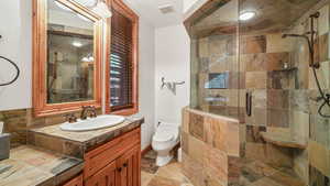 Full bathroom with vanity, a shower stall, and stone tile flooring