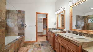 Full bath with stone tile floors, two vanities, and a walk in closet