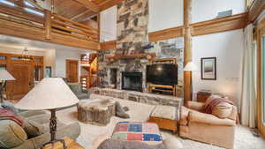 Living area featuring a towering ceiling, a stone fireplace, a wood ceiling with exposed beams, and stairway