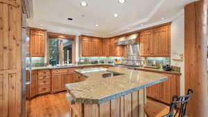 Kitchen featuring light stone counters, wall chimney exhaust hood, light wood-type flooring, backsplash, and recessed lighting