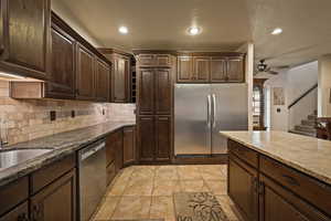 Kitchen with stainless steel appliances, dark brown cabinetry, dark stone countertops, ceiling fan, and recessed lighting