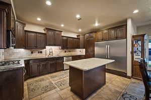 Kitchen featuring dark brown cabinets, appliances with stainless steel finishes, a center island, recessed lighting, and light tile patterned flooring