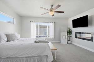 Bedroom with carpet flooring, multiple windows, a glass covered fireplace, ceiling fan, and a textured ceiling