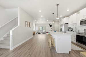 Kitchen with white cabinets, open floor plan, stainless steel appliances, hanging light fixtures, and a breakfast bar