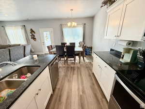 Kitchen with electric range oven, white cabinets, light wood-type flooring, and dark stone countertops