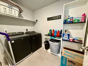 Laundry room with washer and clothes dryer and light tile patterned floors