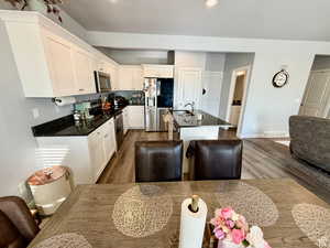Kitchen featuring appliances with stainless steel finishes, a kitchen island with sink, dark stone counters, white cabinetry, and dark wood finished floors