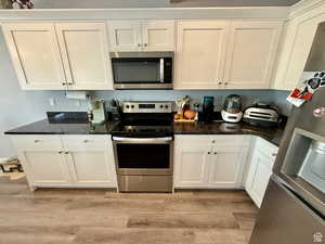 Kitchen featuring stainless steel appliances, white cabinetry, dark stone counters, and light wood finished floors