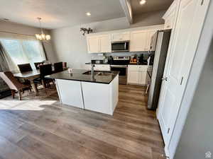 Kitchen with a kitchen island with sink, stainless steel appliances, white cabinets, a chandelier, and decorative light fixtures