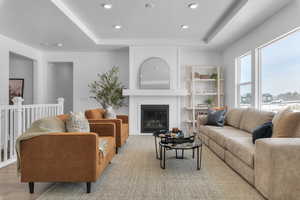 Living room featuring a tray ceiling, a glass covered fireplace, and recessed lighting