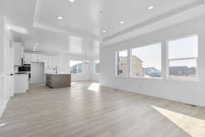 Unfurnished living room with a chandelier, a tray ceiling, recessed lighting, and light wood finished floors