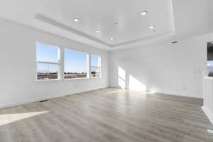 Empty room featuring a tray ceiling, light wood-type flooring, and recessed lighting
