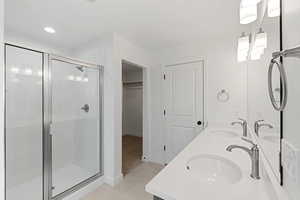 Bathroom with a stall shower, double vanity, a spacious closet, light tile patterned floors, and recessed lighting