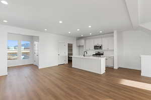 Kitchen with open floor plan, a center island with sink, appliances with stainless steel finishes, white cabinetry, and dark wood-type flooring