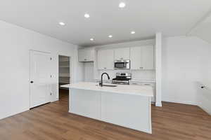 Kitchen featuring appliances with stainless steel finishes, white cabinetry, a kitchen island with sink, recessed lighting, and dark wood-type flooring