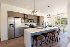 Kitchen featuring appliances with stainless steel finishes, a kitchen breakfast bar, hanging light fixtures, a kitchen island with sink, and gray cabinetry
