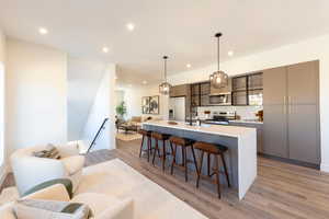 Kitchen with gray cabinets, a large island with sink, open floor plan, pendant lighting, and a kitchen breakfast bar
