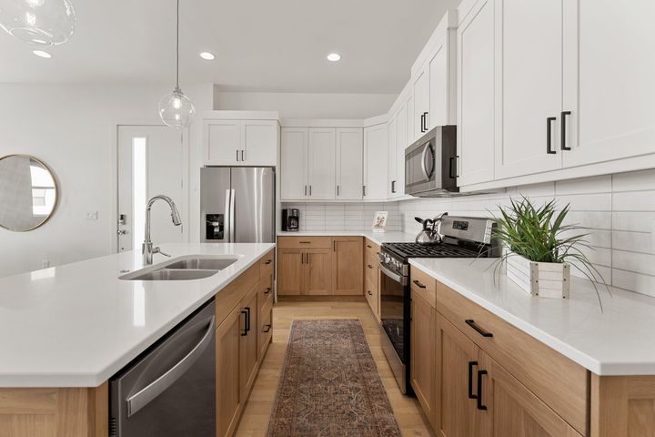 Kitchen with stainless steel appliances, hanging light fixtures, a center island with sink, white cabinetry, and recessed lighting