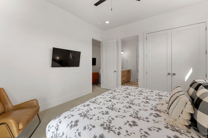 Bedroom with light colored carpet, a closet, a ceiling fan, and ensuite bath