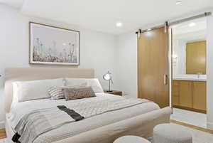 Bedroom with light wood-style floors, a barn door, connected bathroom, and recessed lighting