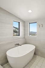 Bathroom featuring a freestanding bath, tile patterned flooring, tile walls, and vaulted ceiling