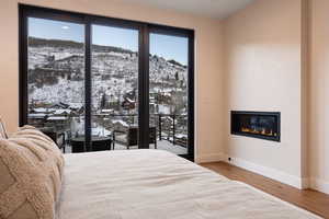 Bedroom featuring a mountain view, a glass covered fireplace, access to outside, and light wood-style floors