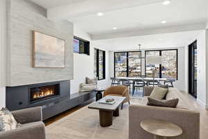 Living room featuring a fireplace, wood finished floors, recessed lighting, beamed ceiling, and expansive windows