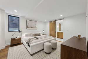 Bedroom with a barn door, light wood-type flooring, recessed lighting, and ensuite bath
