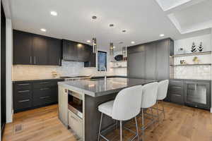 Kitchen featuring open shelves, an island with sink, pendant lighting, wine cooler, and backsplash