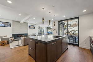 Kitchen featuring dark brown cabinetry, open floor plan, light wood finished floors, hanging light fixtures, and a fireplace