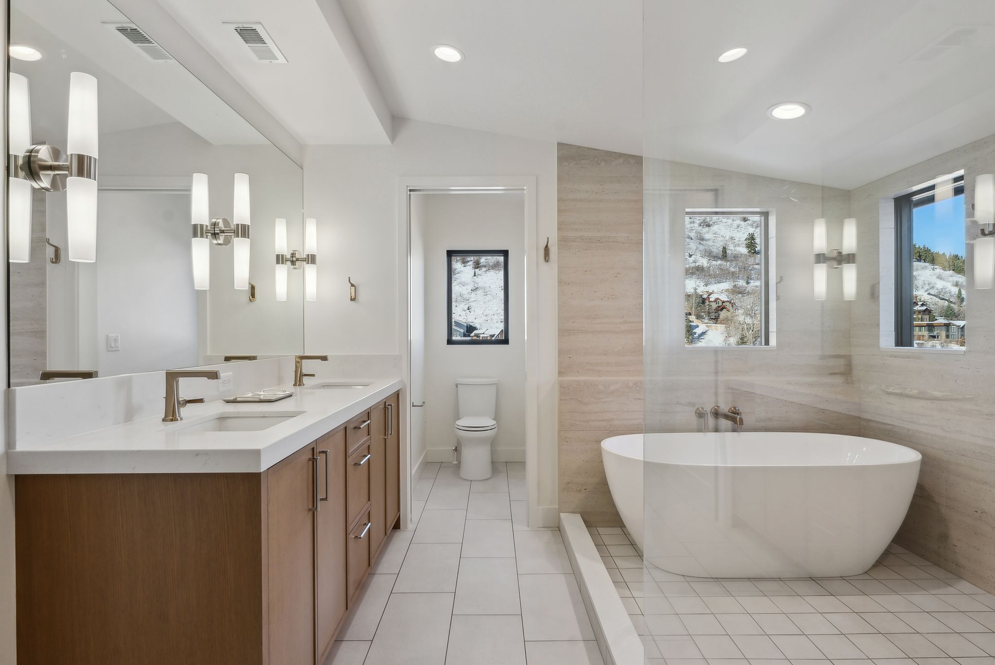 Full bathroom featuring vaulted ceiling, a freestanding bath, double vanity, light tile patterned floors, and recessed lighting