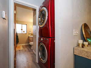 Laundry area featuring stacked washing machine and dryer, a textured wall, and dark wood-style floors