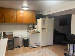 Kitchen featuring brown cabinets, white appliances, light tile patterned flooring, and light countertops